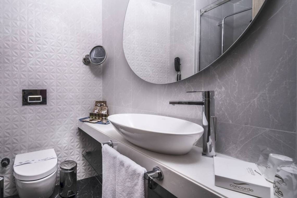Badezimmer im Concorde De Luxe Resort mit weißem Waschbecken, Toilette und Spiegel.