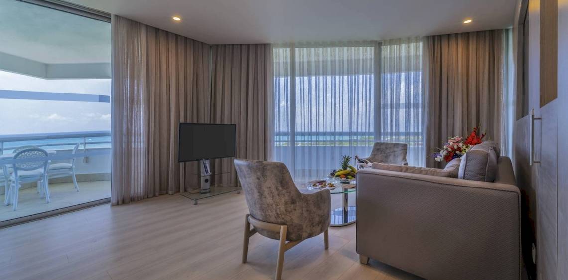 Wohnzimmer im Concorde De Luxe Resort mit Meerblick, Fernseher, Tisch, Stühlen und Balkonmöbeln.