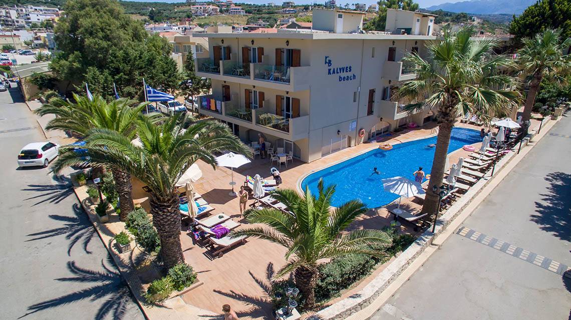 Luftaufnahme des Kalyves Beach Hotels mit Swimmingpool, Sonnenliegen und Palmen.