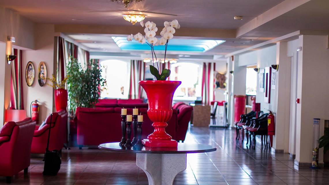 Lobby des Kalyves Beach Hotels mit rotem Vasen-Arrangement und Möbeln.