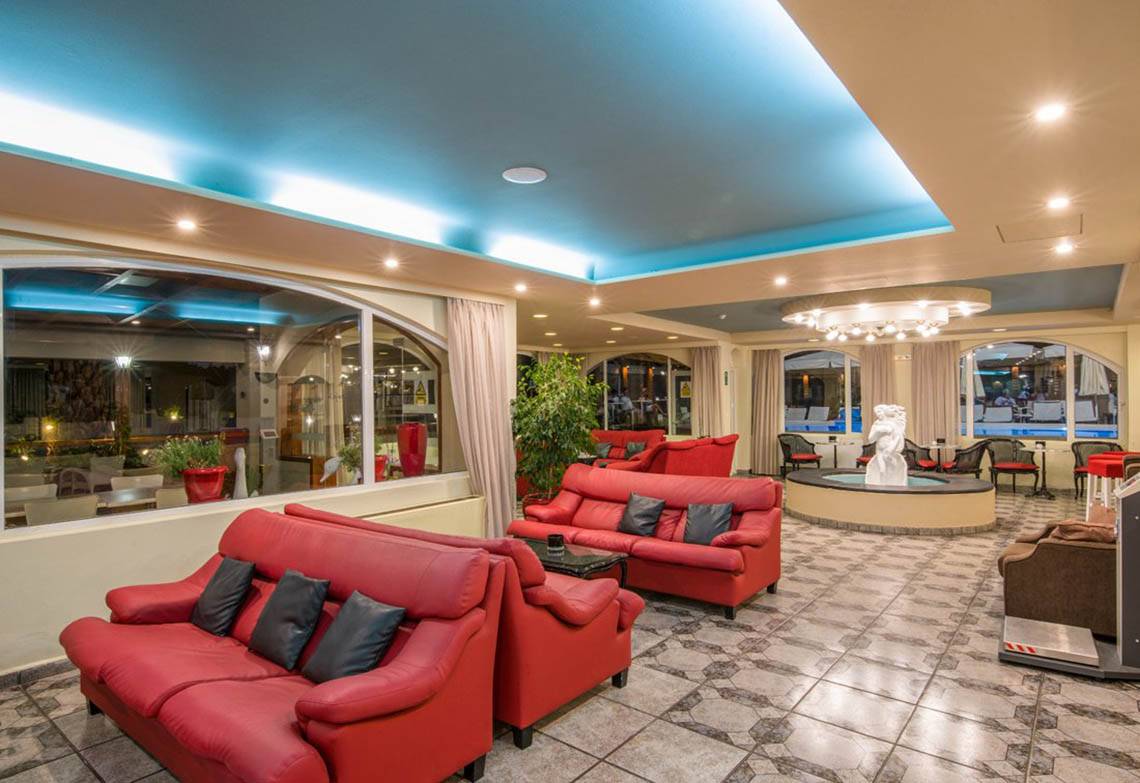 Innenbereich des Kalyves Beach Hotels mit roten Sofas und Tisch, einem Brunnen und einer blauen Decke.