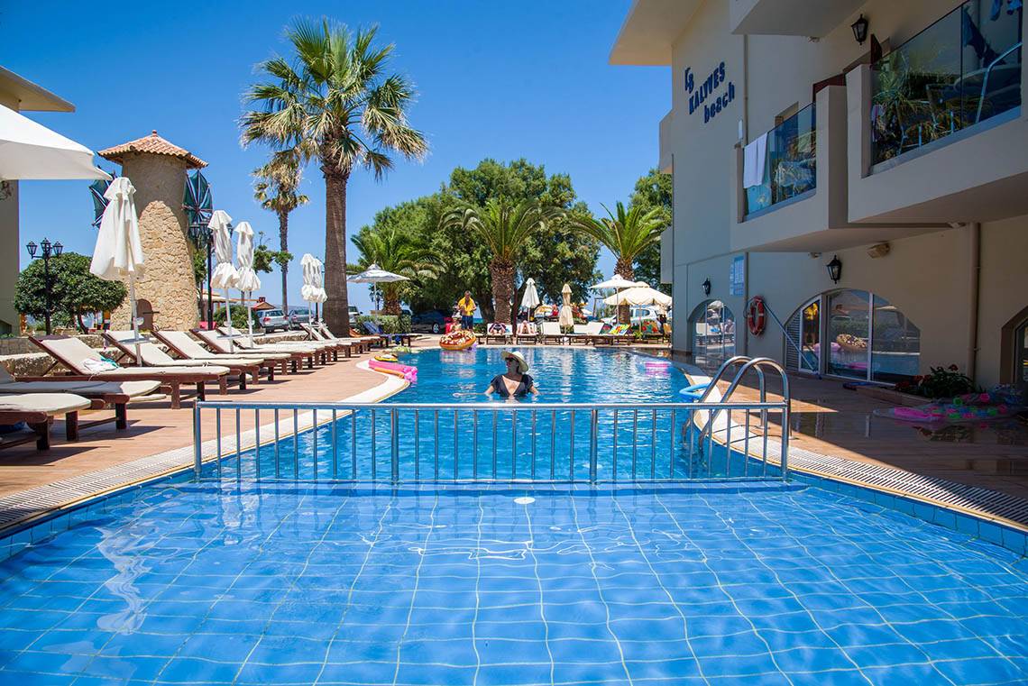 Ein Schwimmbad am Kalyves Beach Hotel mit einer Person im Wasser und Liegestühlen daneben.