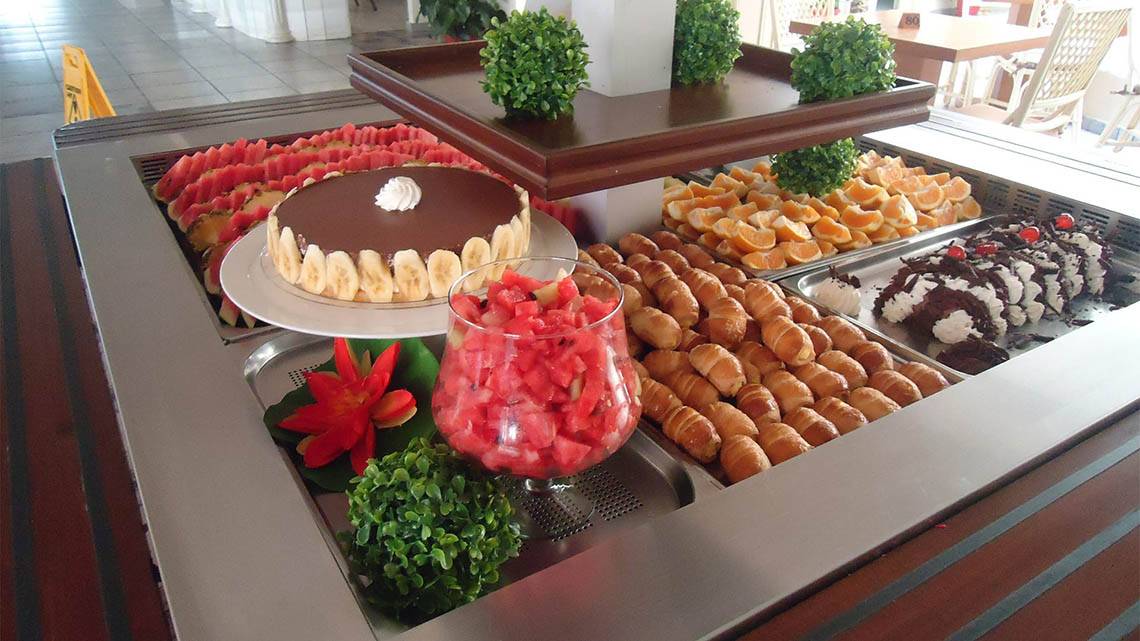 Buffet-Tisch im Kalyves Beach Hotel mit verschiedenen Desserts, Früchten und Getränken.