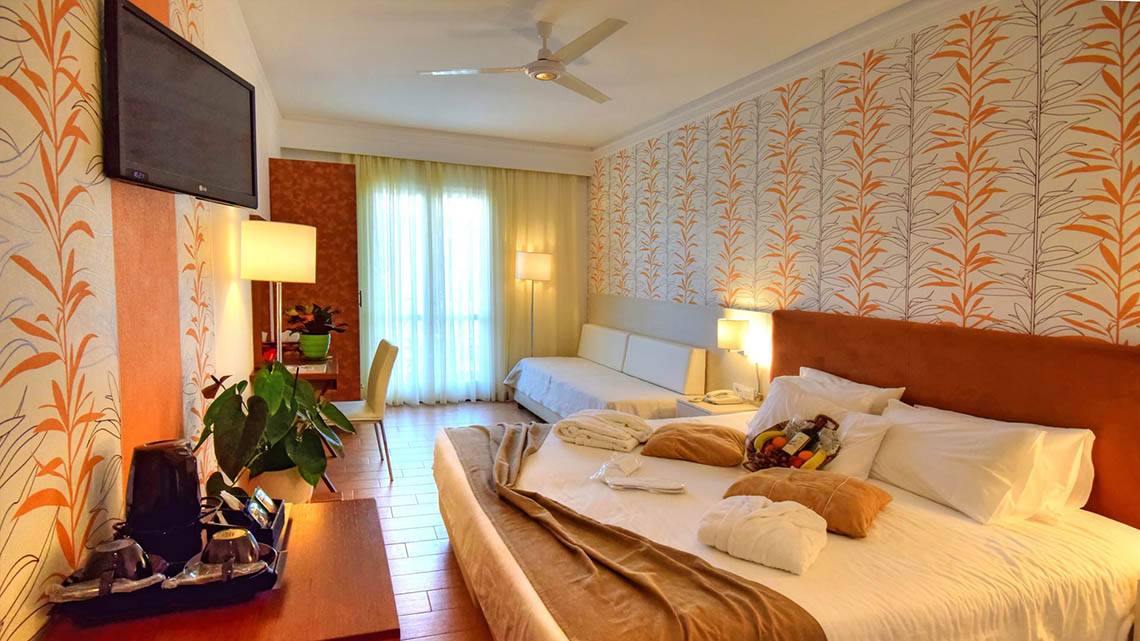 Hotelzimmer im Kalyves Beach Hotel mit Fernseher, Deckenventilator, Bett und Sofa.