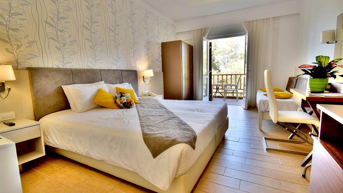 Ein modernes Schlafzimmer im Kalyves Beach Hotel mit einem Doppelbett, Balkonzugang und Wohnzimmermöbeln.