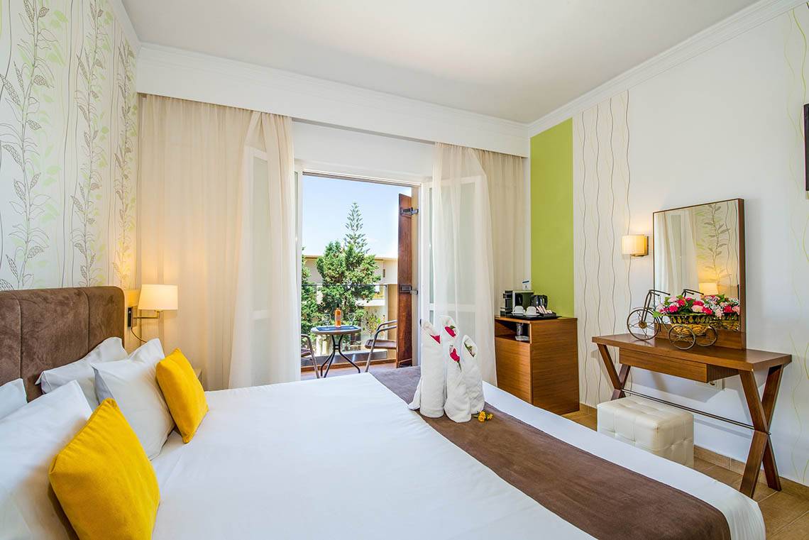 Foto von einem Zimmer im Kalyves Beach Hotel mit einem Bett, Balkon und Blick auf einen Tisch und einen Baum.