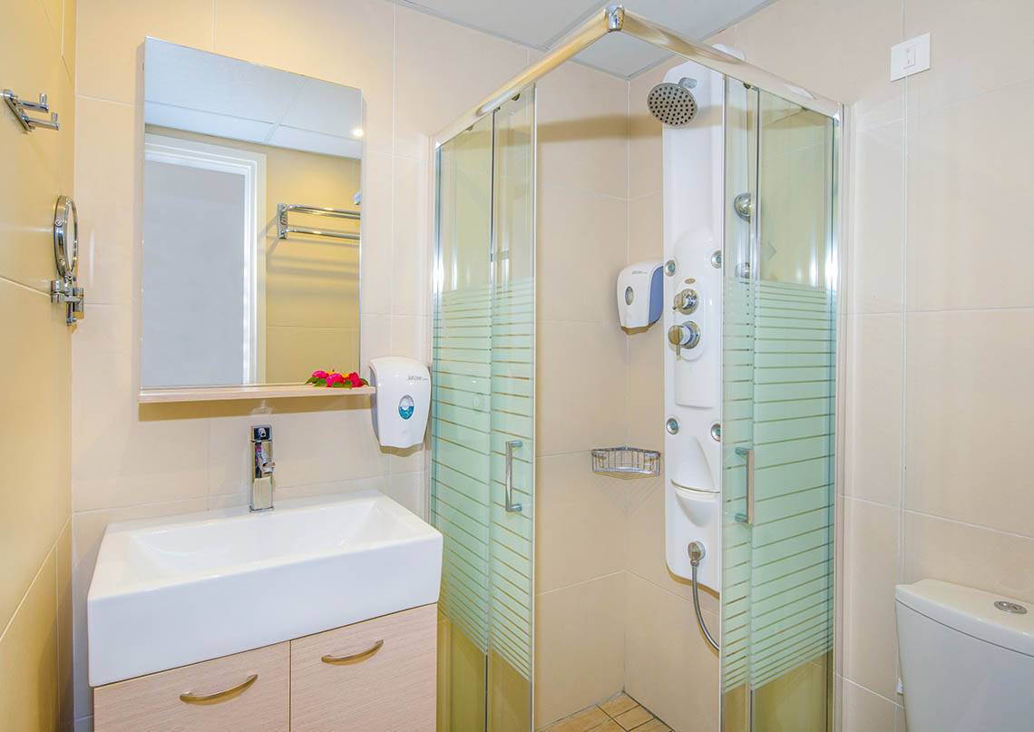 Badezimmer im Kalyves Beach Hotel mit Dusche, Spiegel und Waschbecken.