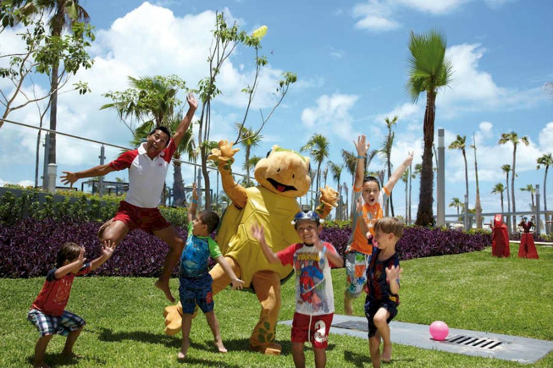 Kinder und ein Mitarbeiter im Riu Palace Peninsula spielen auf der Wiese.