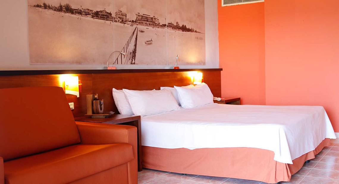 Hotelzimmer im Occidental Arenas Blancas mit Bett, Kissen, Stuhl und Wandmalerei.