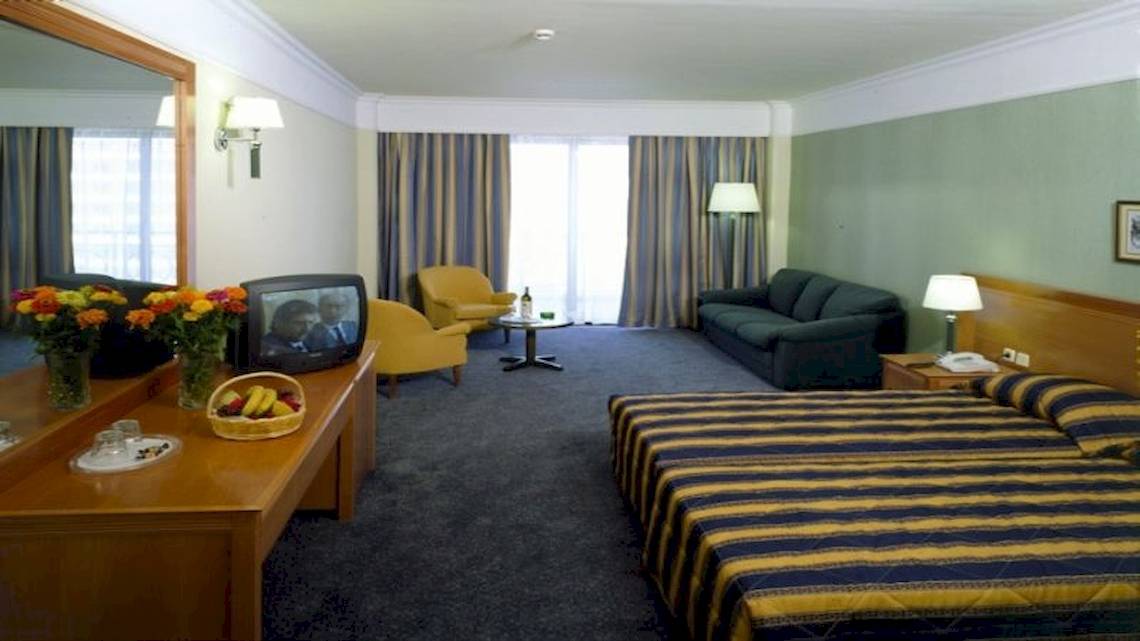 Hotelzimmer des Calypso Palace mit Bett, Fernseher, Couch, Schreibtisch und Spiegel.