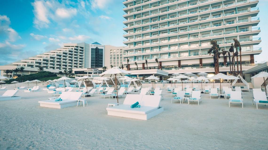 Strand mit weißen Sonnenliegen und Sonnenschirmen vor dem Coral Level at Iberostar Selection Cancun Hotel
