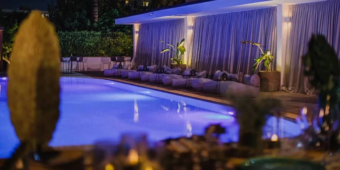 Poolbereich des Alion Beach Hotel bei Nacht mit blauer Beleuchtung und Loungemöbeln.