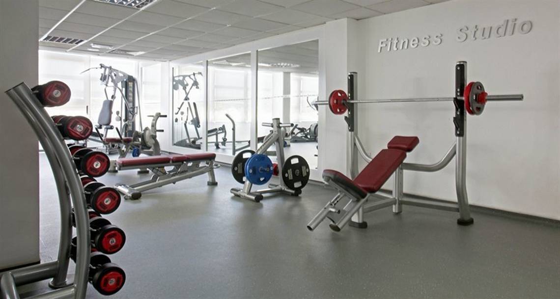 Fitnessstudio im Alion Beach Hotel mit verschiedenen Geräten und einer weißen Wand.