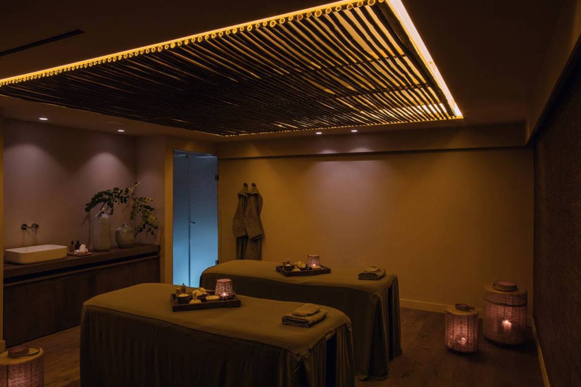 Massageraum im Alion Beach Hotel mit zwei Behandlungstischen und dekorativen Lampen.