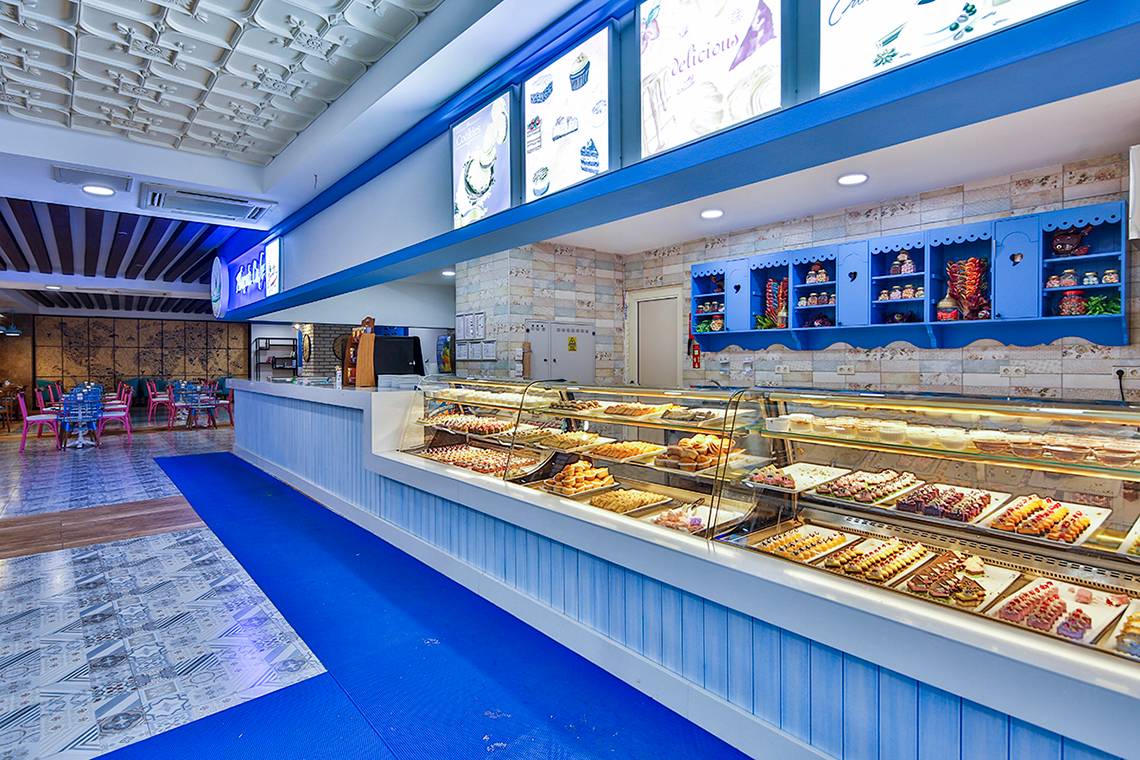 Innenansicht des Cafes im Crystal Admiral Resort Suites & Spa mit Kuchen und Gebäck auf dem Tresen