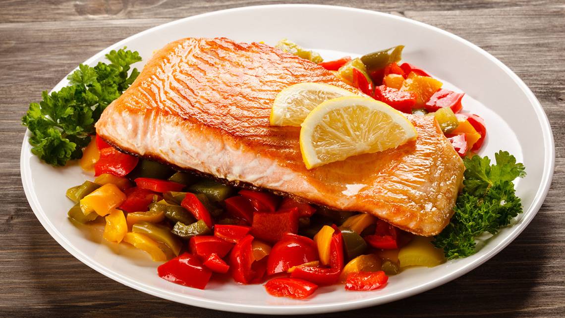 Ein Teller mit gebratenem Lachs, Zitrone und buntem Gemüse.