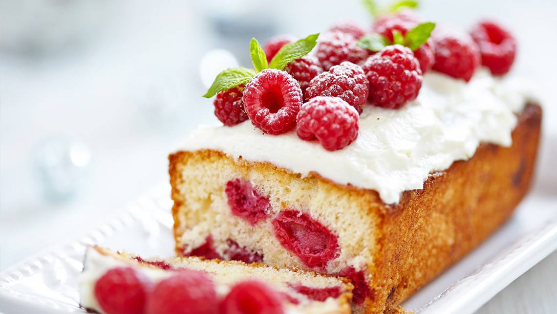 Ein Kuchen mit Himbeeren und weißer Creme auf einem weißen Teller.