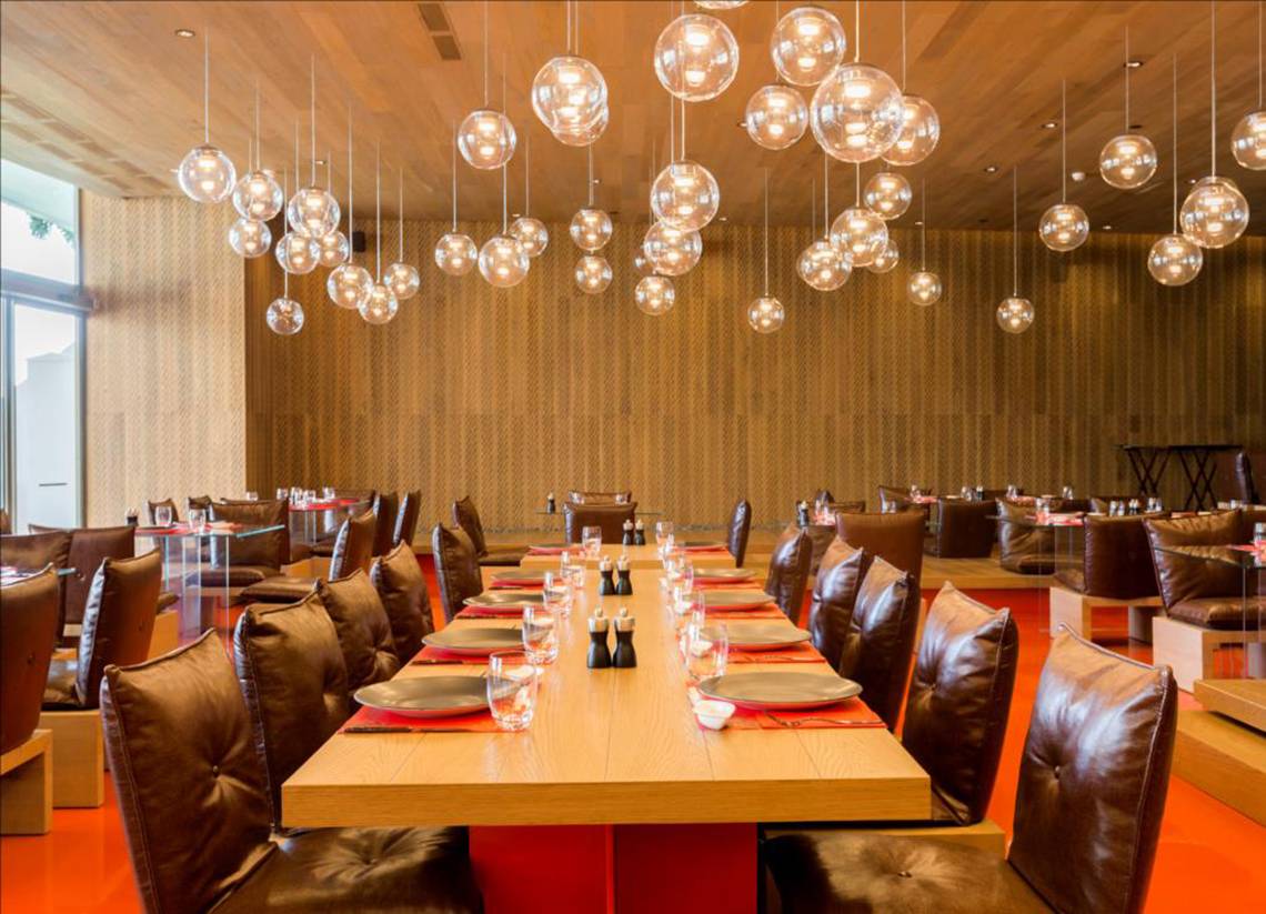 Innenansicht des Restaurants im Maxx Royal Belek Golf Resort mit langen Tischen, Lederstühlen und runden Lampen an der Decke.