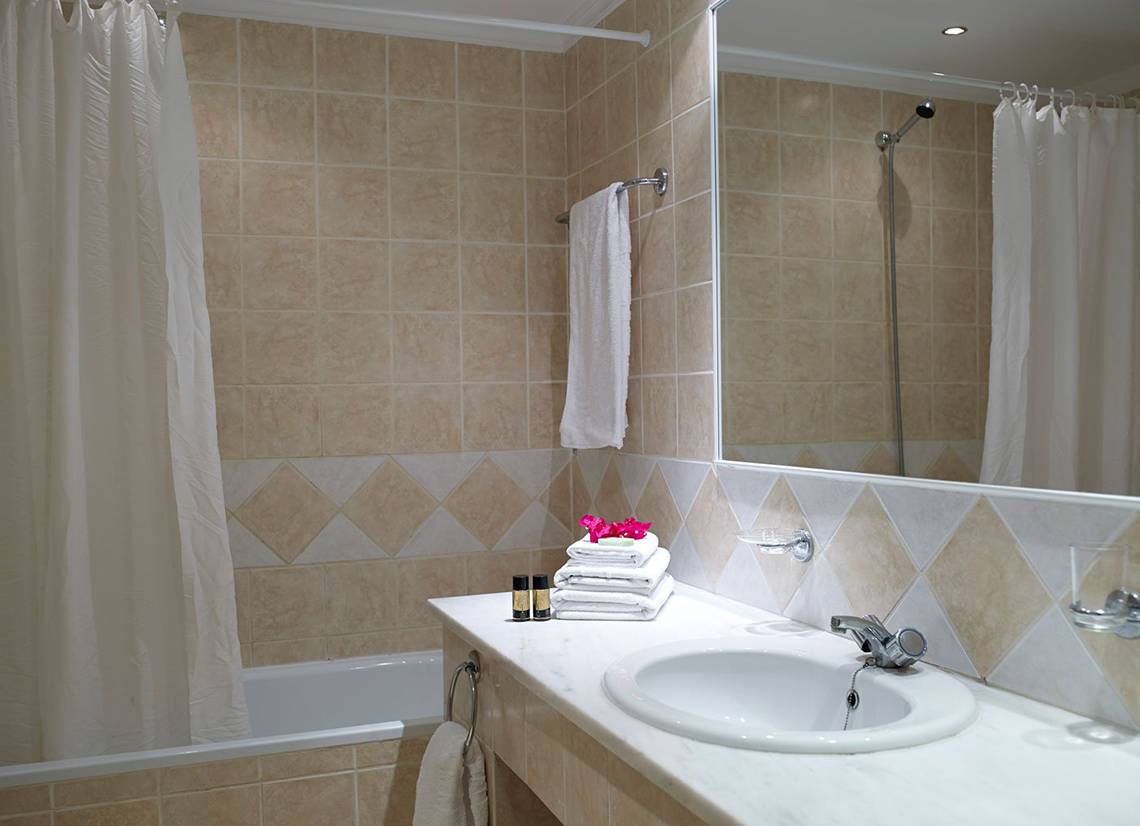 Badezimmer im Mitsis Family Village Beach Hotel mit Badewanne, Waschbecken und Handtüchern