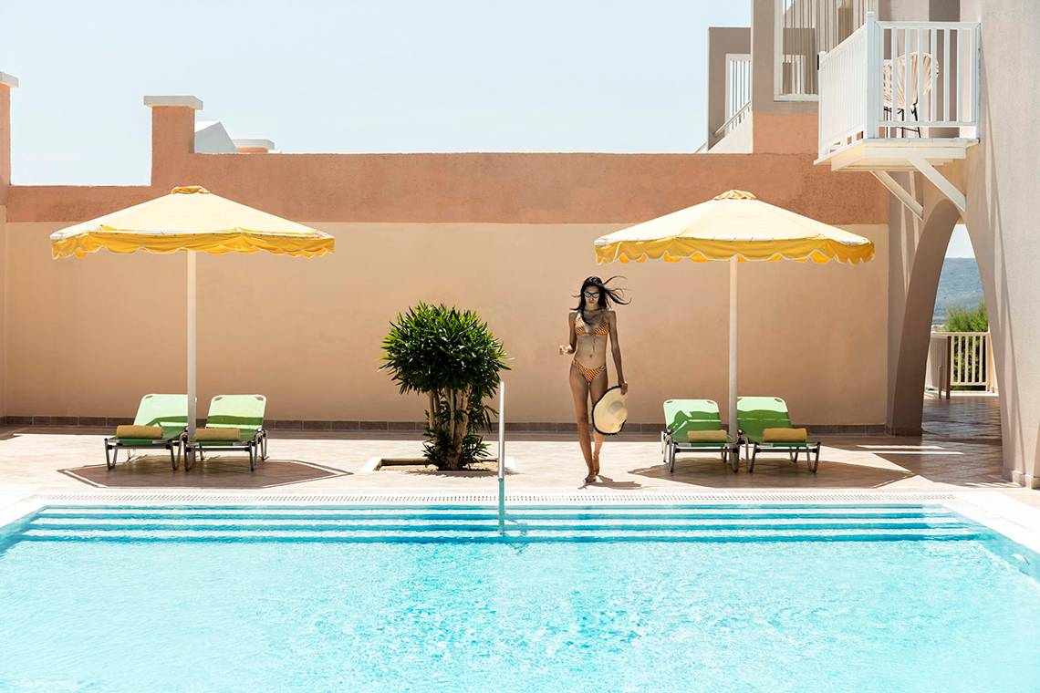 Eine Frau am Pool mit gelben Umbrellas und grünen Liegen im Mitsis Family Village Beach Hotel.