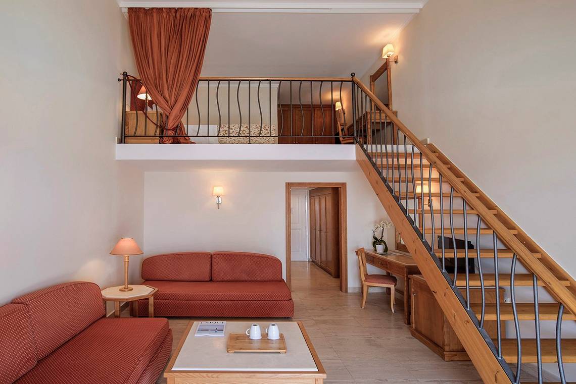 Innenansicht der Suite im Mitsis Family Village Beach Hotel mit Wohnzimmer, Schlafbereich und Treppe.