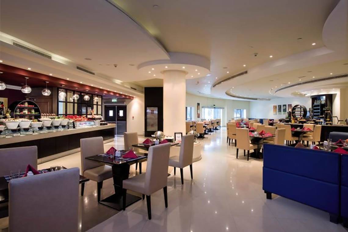 Innenansicht des Restaurants im Al Hamra Residence Hotel mit gepolsterten Stühlen und Tischen.