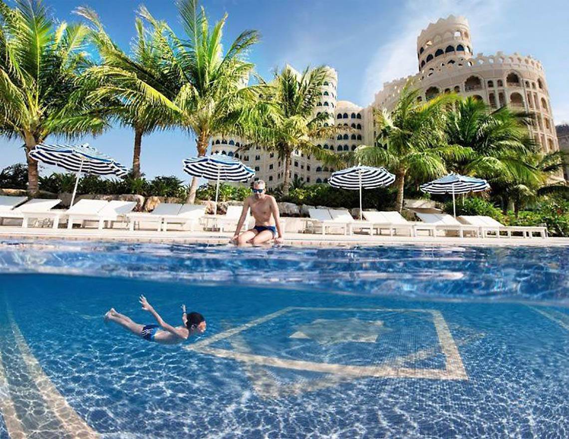 Mann und Kind schwimmen im Pool des Al Hamra Residence Hotels.