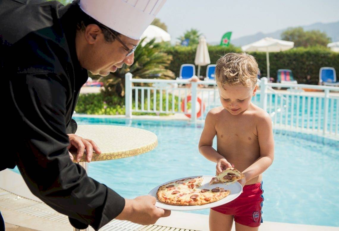 Koch gibt einem jungen Jungen eine Pizza am Pool im Mediterranean Beach Resort.