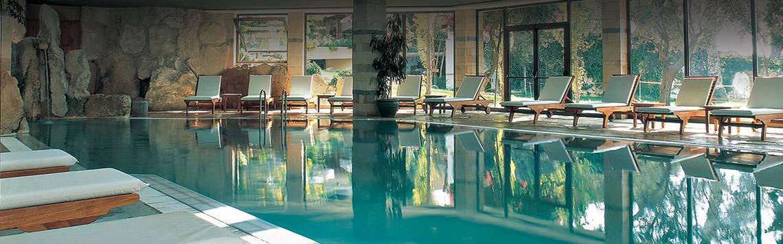 Innenpool des Coral Beach Hotel & Resorts mit Lounge-Sesseln und Pflanzen.
