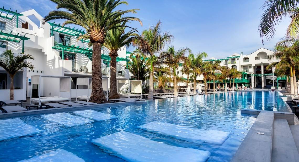 Ein großer Swimmingpool mit weißen Liegen und Palmen im Barceló Teguise Beach Adults Only Hotel.