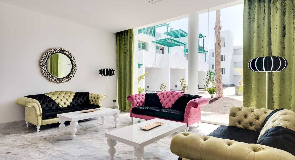 Hotelloungebereich des Barceló Teguise Beach mit bunten Sofas, Tisch und spiegelverzierten Wänden.