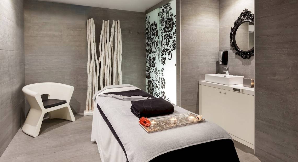 Spa-Behandlungsraum im Barceló Teguise Beach Adults Only Hotel mit Liege, Stuhl und Waschbecken.