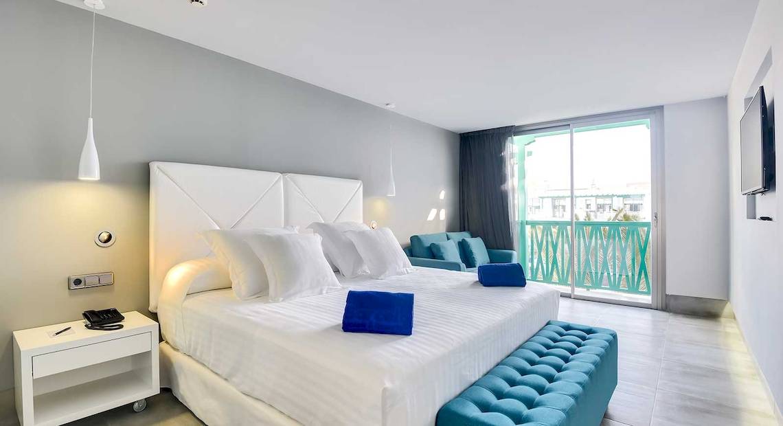 Modernes Hotelzimmer im Barceló Teguise Beach Adults Only mit weißem Bett, blauen Kissen und grünem Balkon.