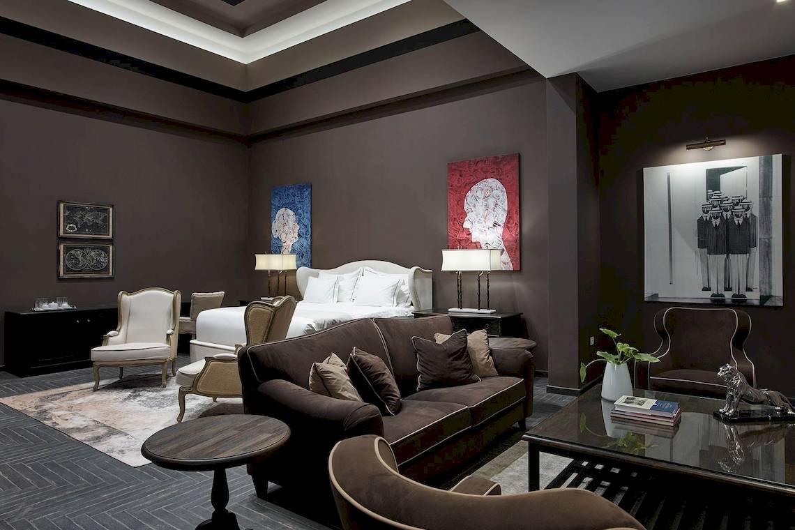 Schlafzimmer des Pelagos Suites Hotel mit Bett, Sofa, Lampen und Gemälden an der Wand.