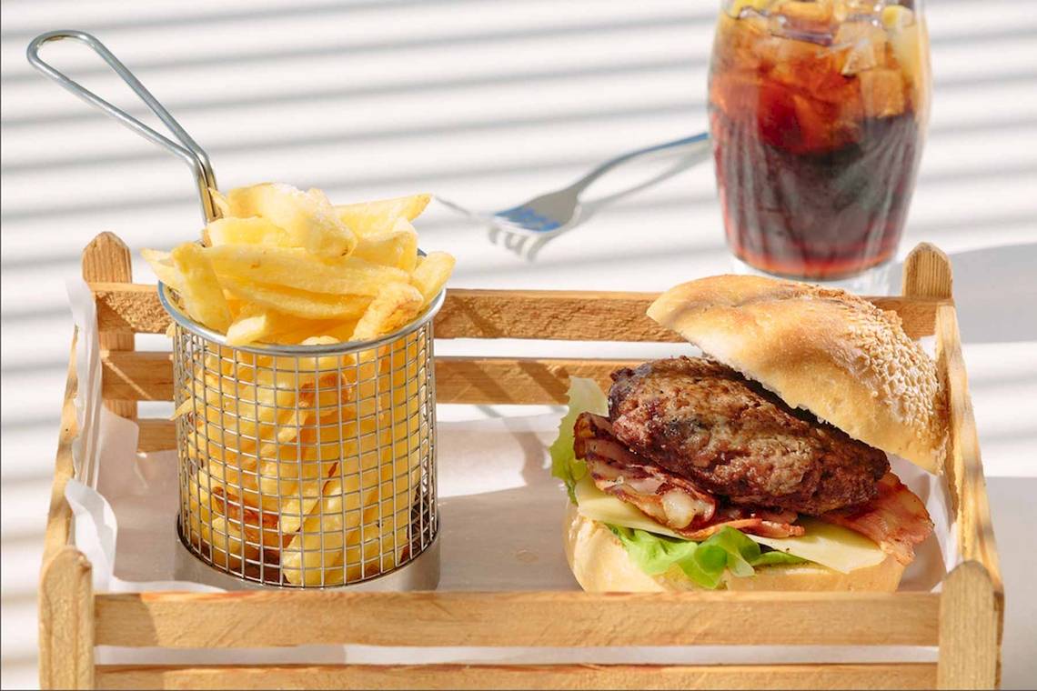 Ein Holztablett mit einem Burger, Pommes und einem Glas Cola.