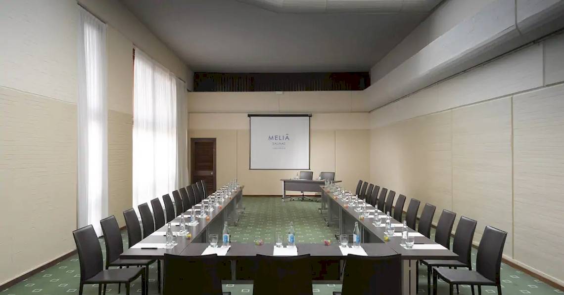 Konferenzraum im Melia Salinas Hotel mit langen Tischen und Stühlen, Projektionsleinwand und Möbeln.