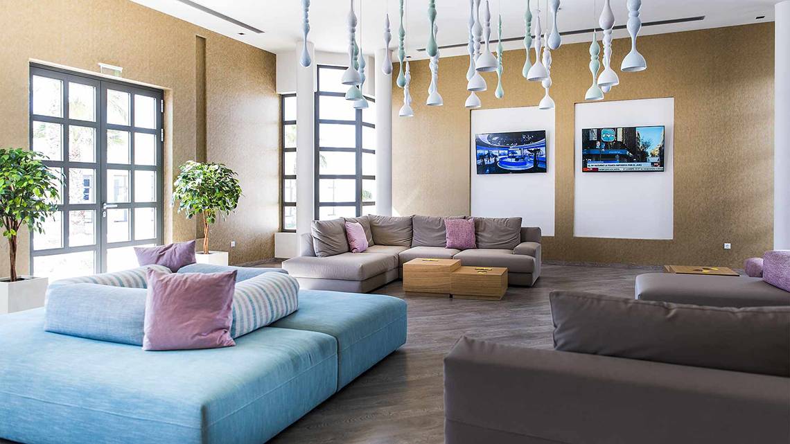 Lobby-Lounge des Club Plimmiri Hotels mit Sofas, Fernsehern und Pflanzen.