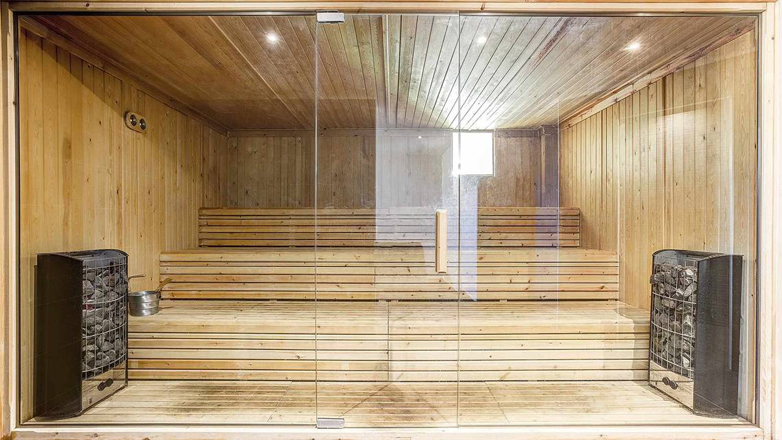 Innenansicht der Sauna im Club Plimmiri mit Holzbänken und Glaswänden.