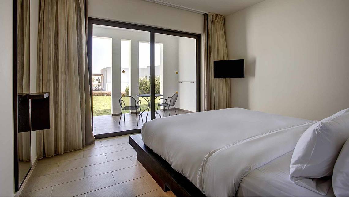 Ein Zimmer im Club Plimmiri Hotel mit einer Terrasse, auf der zwei Stühle und ein Tisch stehen, und einem großen Bett.