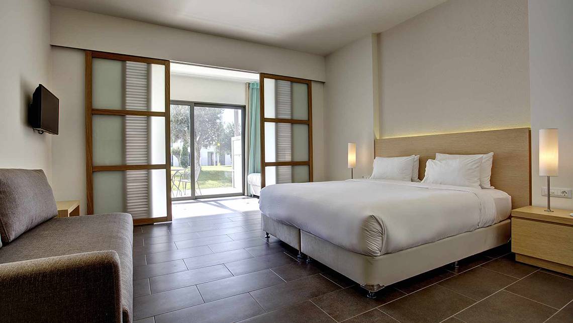 Innenansicht eines Zimmers im Club Plimmiri Hotel mit Doppelbett, Sofa, Tisch und modernem Design.