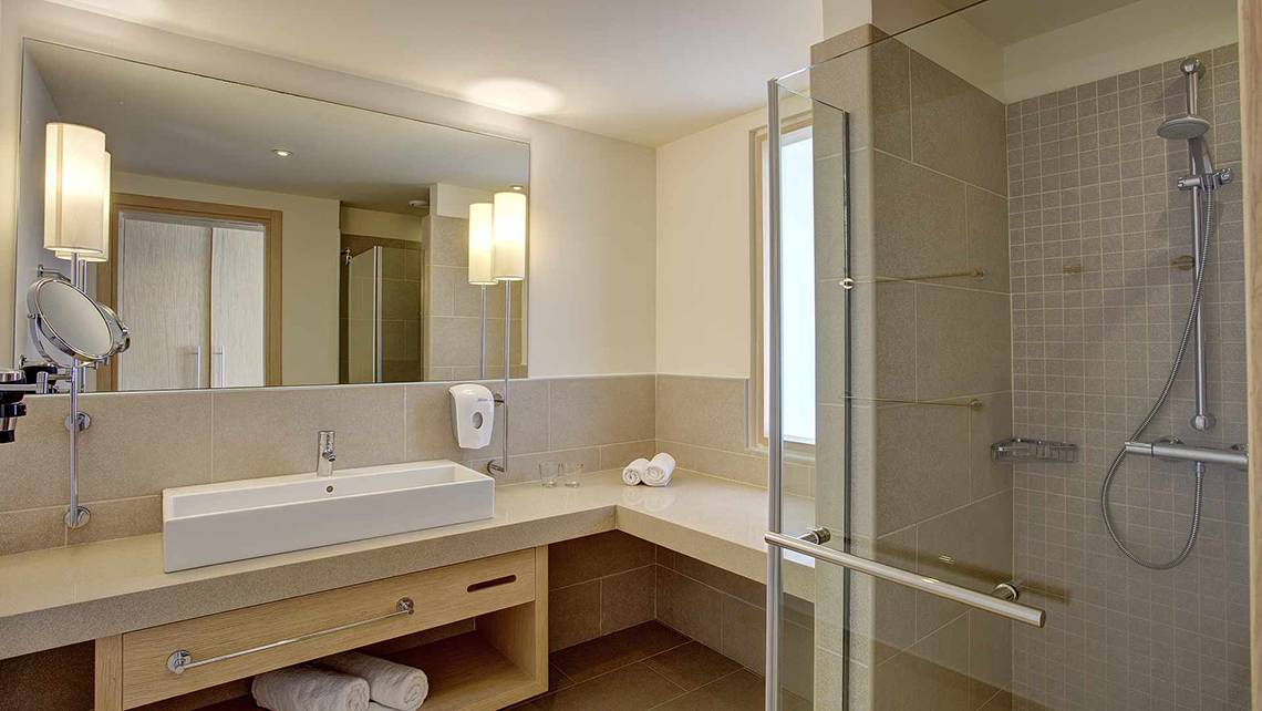Badezimmer im Club Plimmiri Hotel mit Spiegel, Waschbecken, Dusche und Handtüchern.