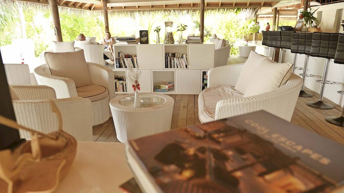 Loungebereich im Outrigger Maldives Maafushivaru Resort mit weißen Möbeln und Büchern.