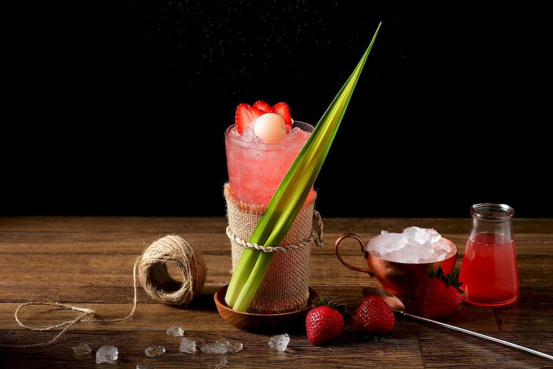 Ein roter Cocktail in einem Glas mit Eis und einer Strohhalm auf einem Holztisch.