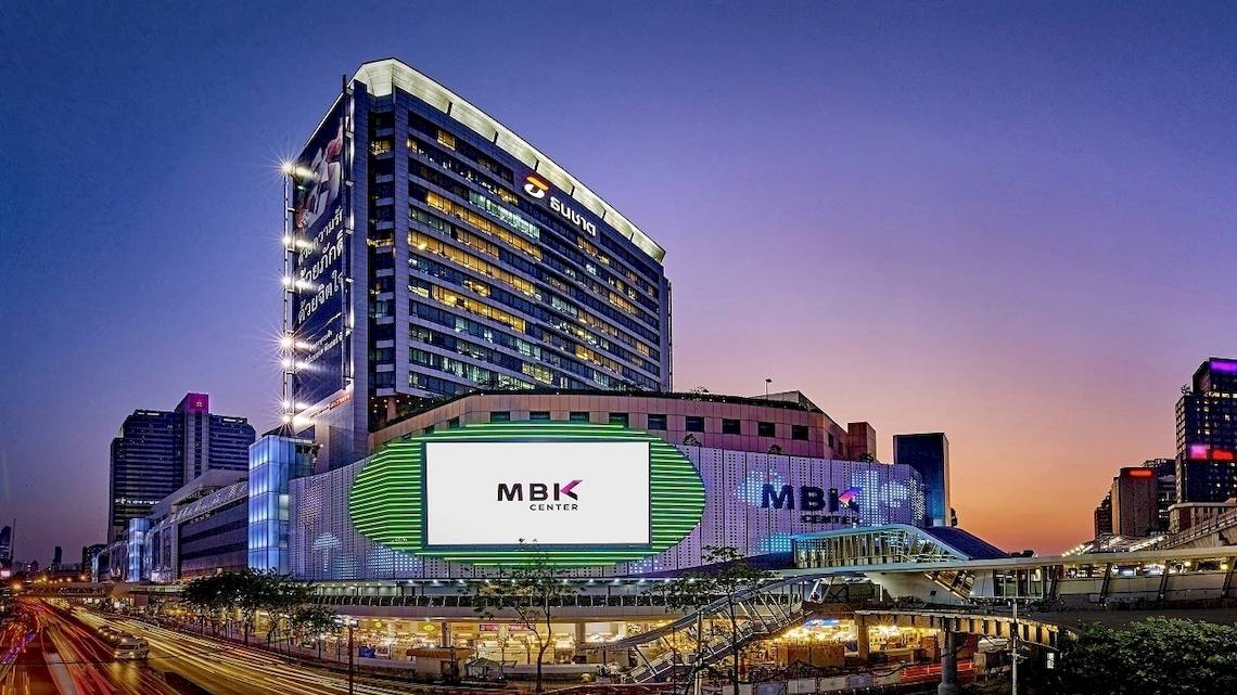 Nachtansicht des Pathumwan Princess Hotels mit Beleuchtung und großen Anzeigetafeln.