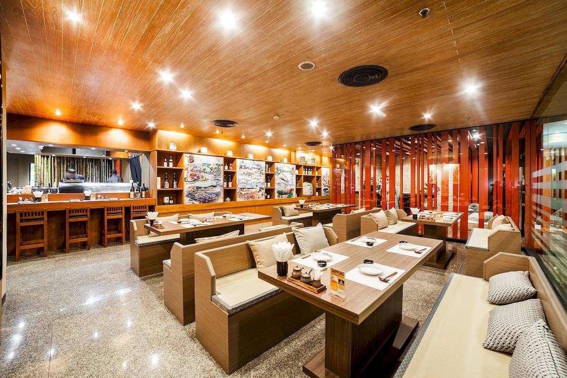 Innenbereich des Pathumwan Princess Hotels mit gepolsterten Sitzbänken, Holztischen und Bar.