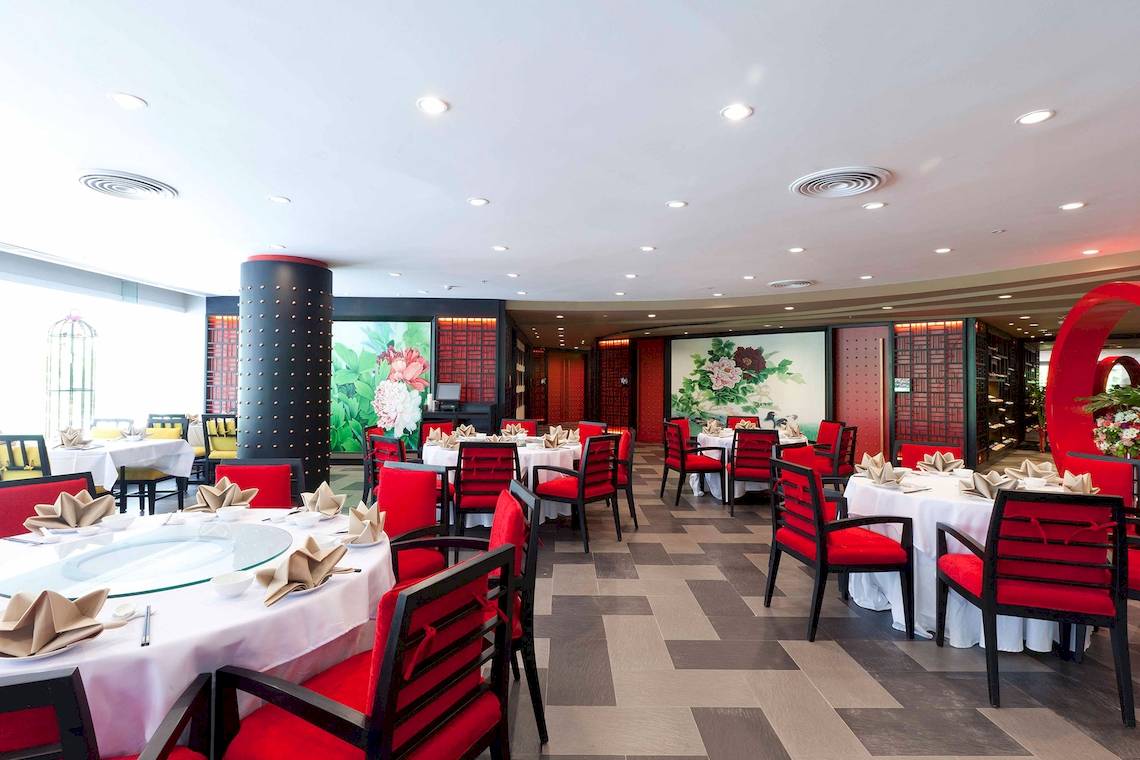 Innenansicht des Restaurants im Pathumwan Princess Hotel mit roten Stühlen und Tischdecken.
