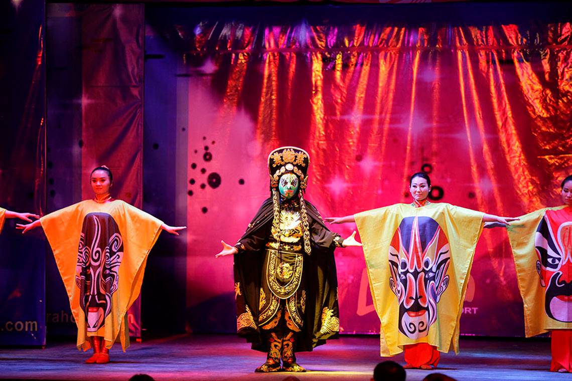 Fünf Personen in traditionellen Kostümen und Masken führen eine Bühnenshow auf.