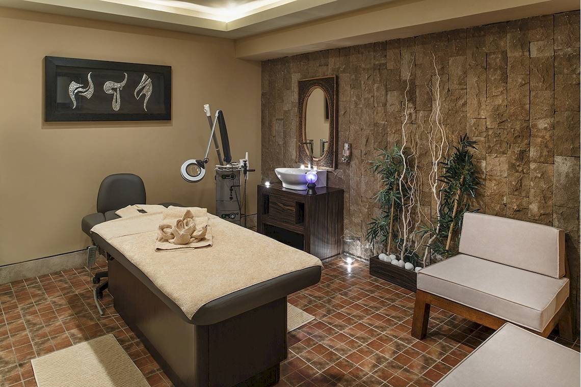 Massageraum im Voyage Torba Hotel mit Behandlungstisch, Spiegel und Pflanzen.