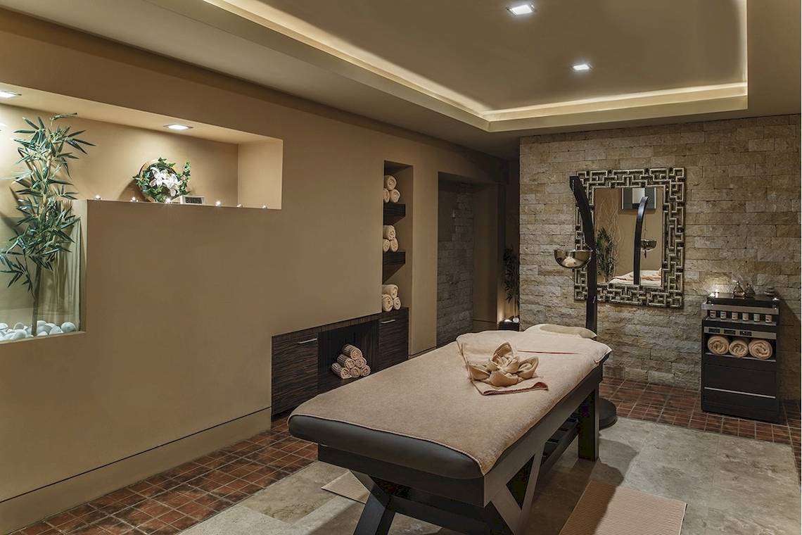 Spa-Behandlungsraum im Voyage Torba Hotel mit Massagetisch, gerollten Handtüchern, und dekorativen Elementen.