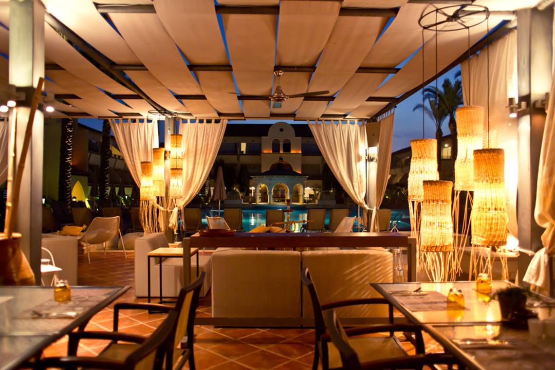 Abendaufnahme des Restaurants im Napa Plaza Hotel mit Außenbereich, Tischen und Stühlen unter einem Dach mit Vorhängen und Lampen.